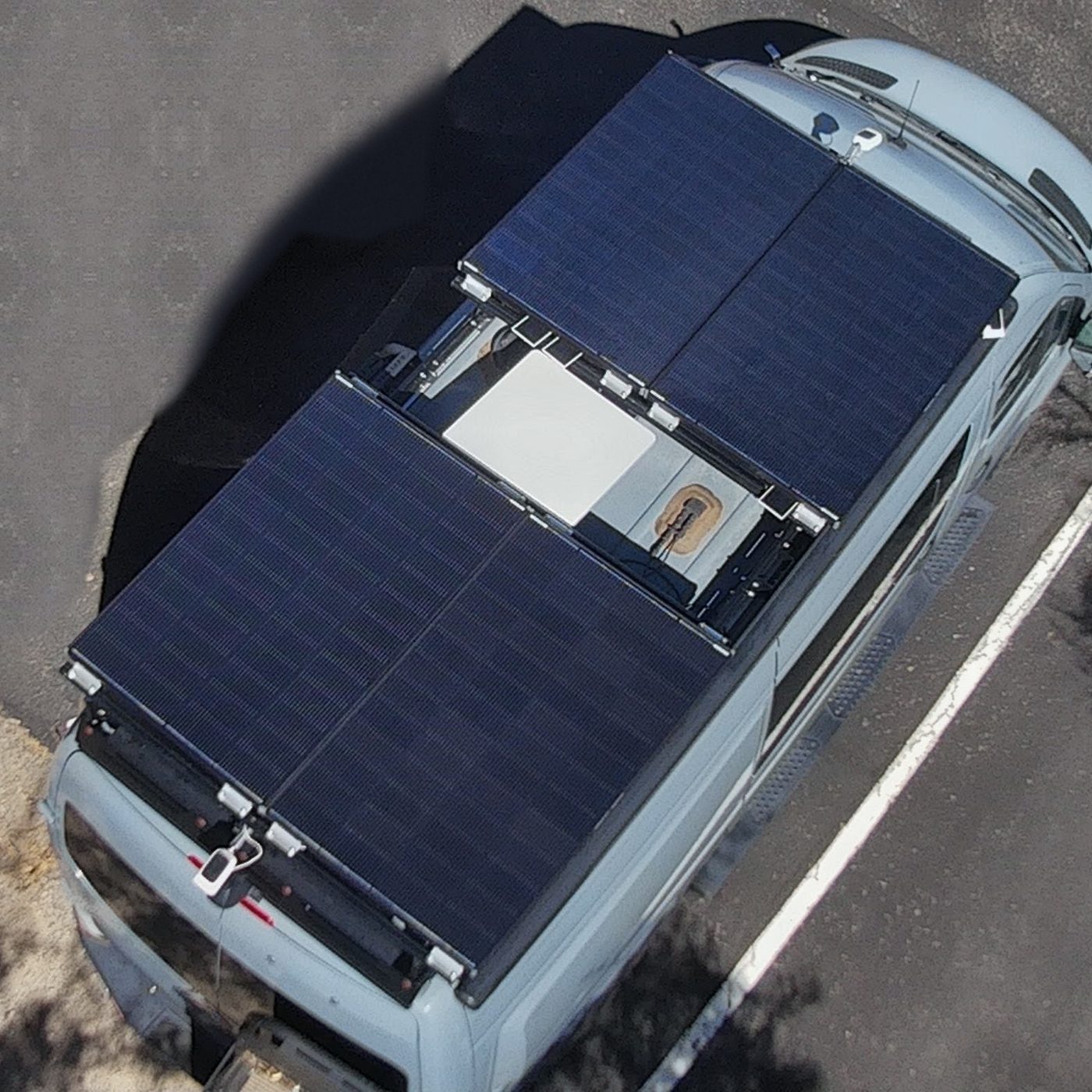 Overhead view of a van roof with four solar panels and a satellite dish mounted between the front and rear pairs